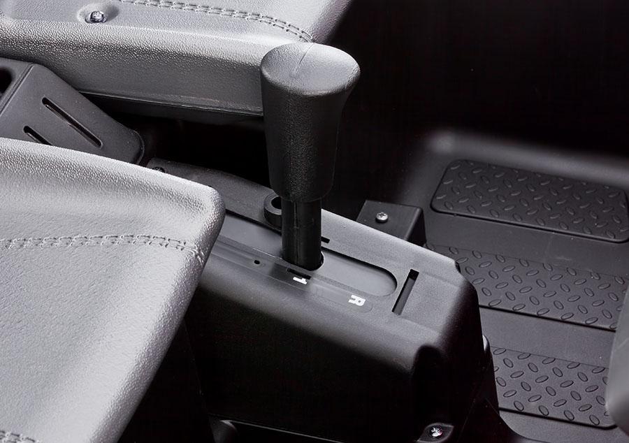 Close-up of black gear shifter and textured floor mat with stitched bucket seat inside a camo ride-on vehicle cockpit