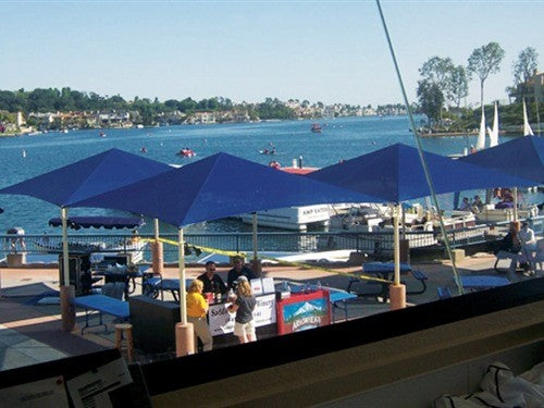 Pyramid Roof Shade Structure with blue fabric and four posts providing UV protection over lakeside picnic area