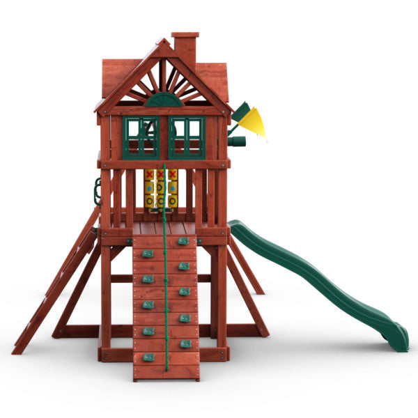 Redwood-finished wooden playset with climbing wall, tic-tac-toe panel, green wave slide, and upper clubhouse with shutters and chimney