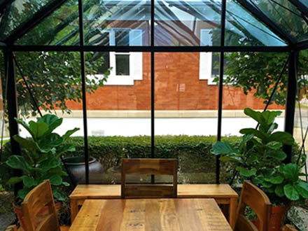 Dark green classic English-style greenhouse interior with wooden table, chairs, and lush potted plants