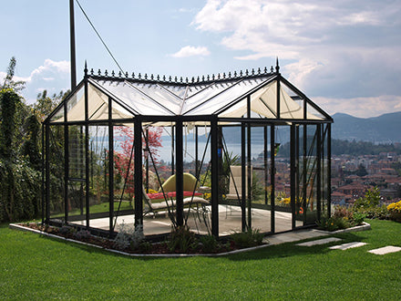 Royal Victorian Orangerie Greenhouse with dark green aluminum frame, tempered glass panels, decorative roof cresting, and double sliding door in garden setting