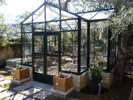 Classic dark green aluminum-framed greenhouse with tempered glass panels, roof and louvre windows, and double sliding door