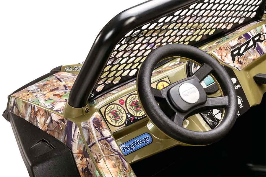 Close-up of camo-patterned kids' ride-on vehicle dashboard with steering wheel, gauges, mesh roll bar, and horn button.