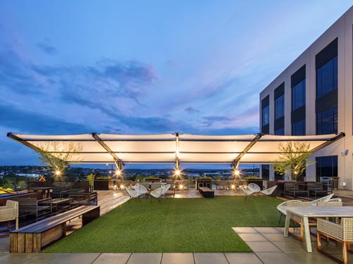 Slanted Cantilever Wing Cabled Shade Structure with tilted fabric top and two grey columns over rooftop patio seating at dusk