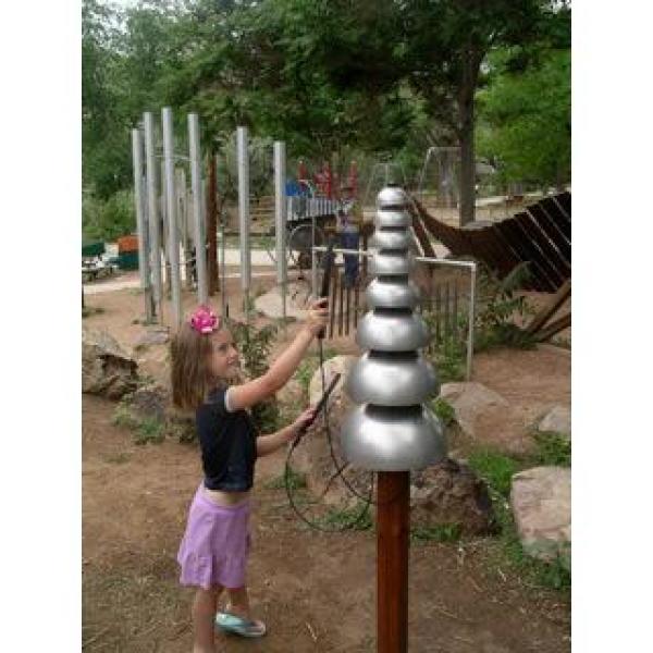 Child playing vertical silver aluminum outdoor musical instrument with tiered bells on wooden post in park setting