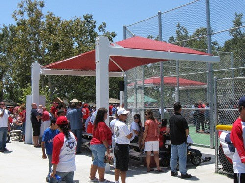 Rectangular cantilever hip roof shade structure with red fabric covering picnic benches near sports court