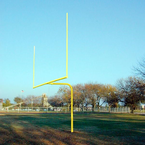 Yellow single bent steel football goal post on grassy field under clear blue sky with trees in background
