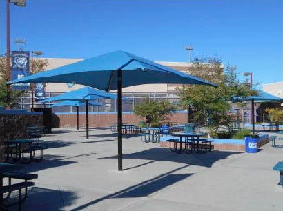 Single Post Pyramid Roof Shade Structure with blue UV-blocking fabric over outdoor picnic tables in a sunny playground setting