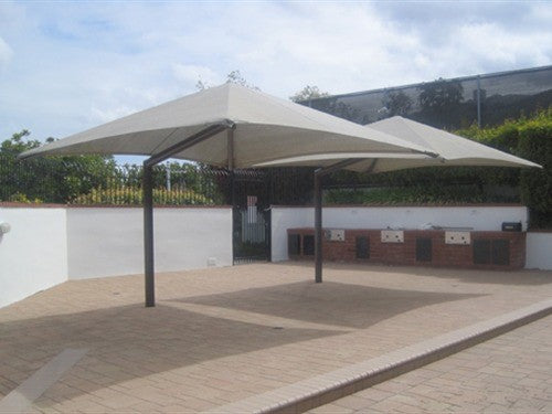 Two beige single post pyramid cantilever shade structures providing UV protection over paved area with built-in grills
