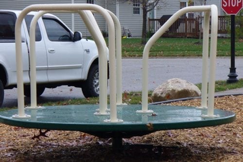 Green powder-coated steel merry go round with white handrails on wood chip playground surface