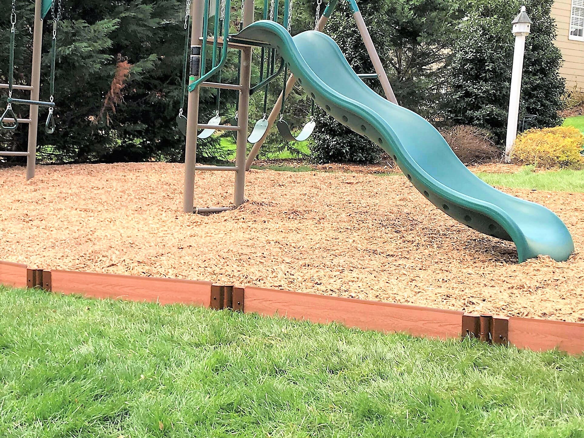 Tool-Free Classic Straight Playground Border in sienna containing wood chip safety surfacing around green slide and swings in backyard playground