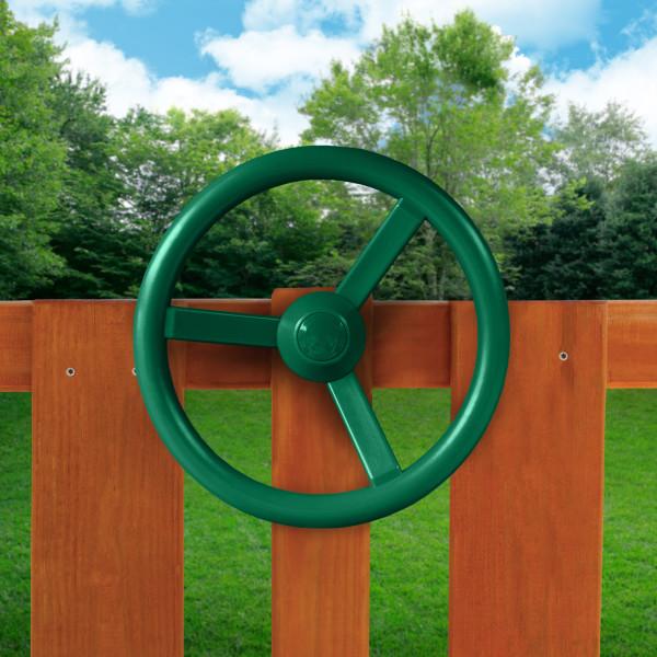 Green plastic steering wheel mounted on amber-stained cedar wood fence panel outdoors with greenery background