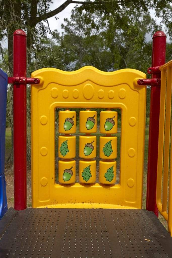 Yellow playground panel with rotating blocks featuring acorn and leaf illustrations on a colorful play structure.