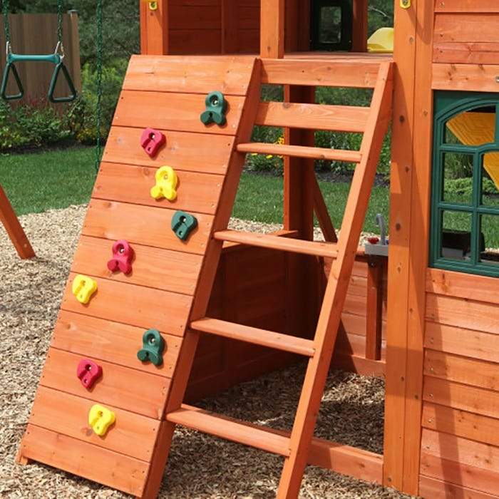 Wooden outdoor playset with multi-colored climbing rockwall, wooden ladder, green window frame, and attached swings
