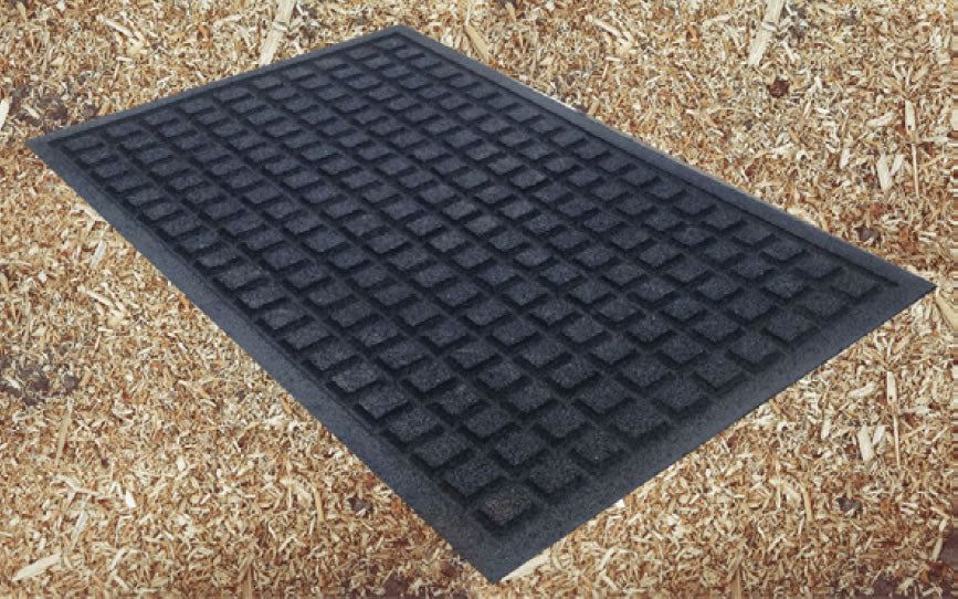 Black heavy-duty rubber playground mat with waffle texture and beveled edges on wood mulch surface