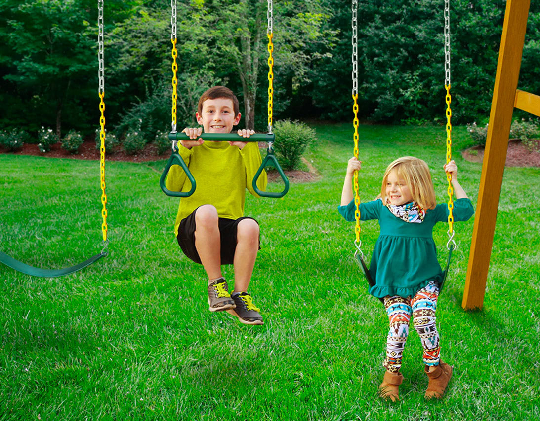 Two children on a wooden swing set with yellow chains and green seats in a grassy backyard