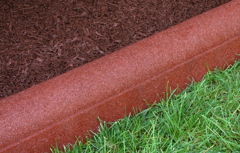 Rounded redwood-colored rubber playground border timber with textured surface and engineered drainage ports separating mulch and grass