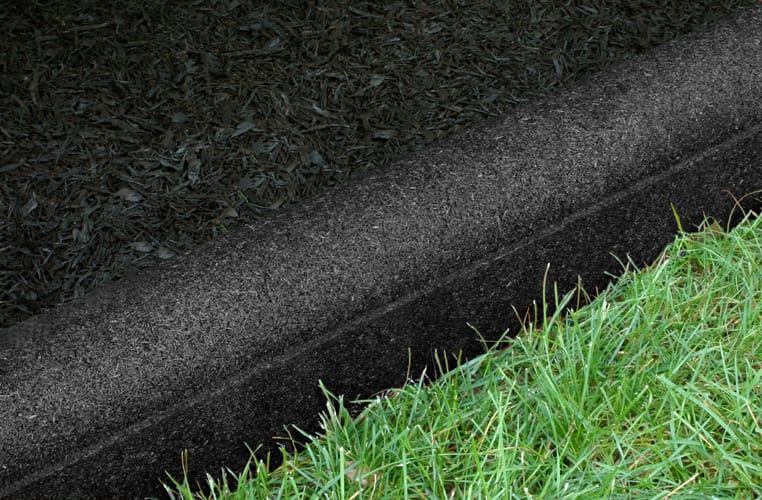 Rubberific Playground Border Timbers in black, flexible rubber edging between grass and mulch with rounded top and drainage ports