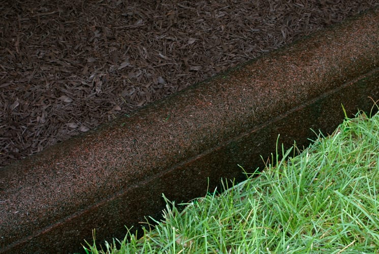 Earthtone brown flexible rubber playground border timber with rounded top separating mulch and grass.