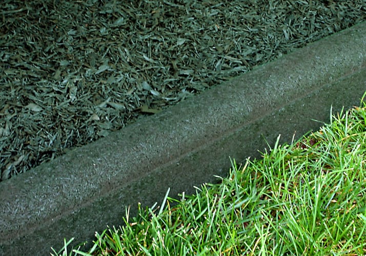 Forest green flexible rubber playground border timber with rounded top separating mulch and grass.