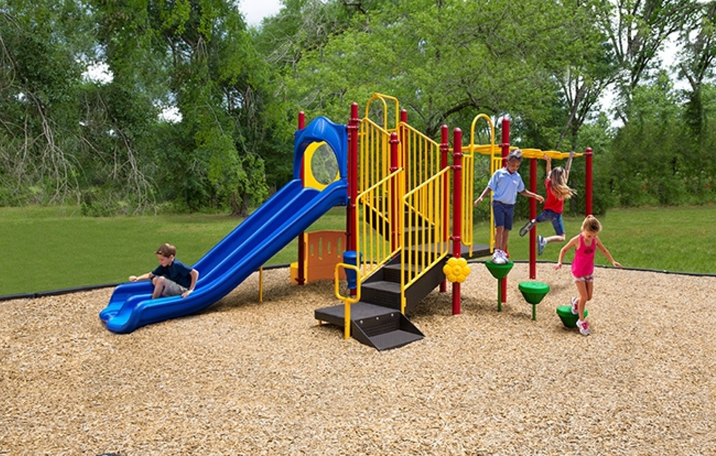 Colorful playground with double blue slide, yellow railings, monkey bars, climbing pods, and wood chip surface