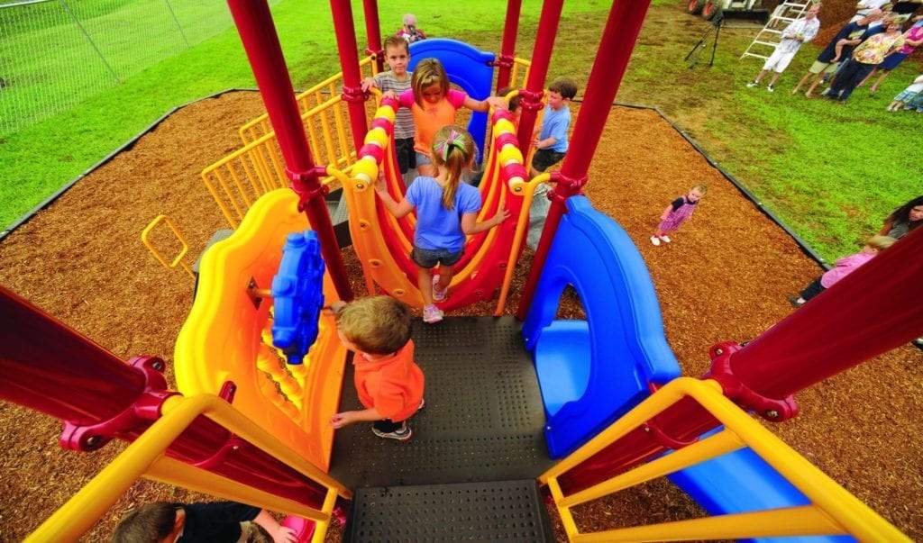 Children playing on colorful playground structure with dual roofs, twisting slides, climbing elements, and bone bridges.