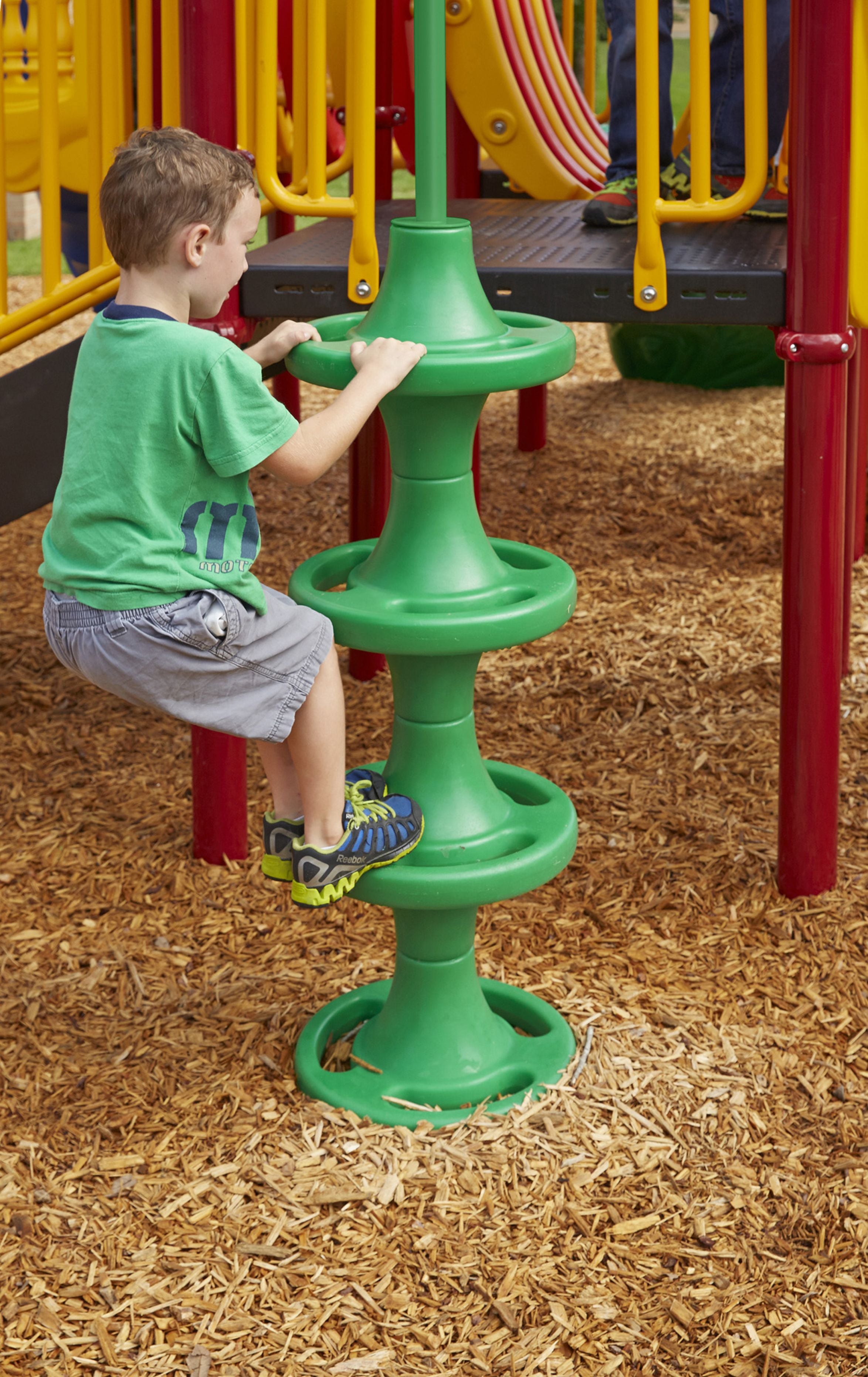 Child climbing green spiral pole on colorful playground with wood chip ground cover