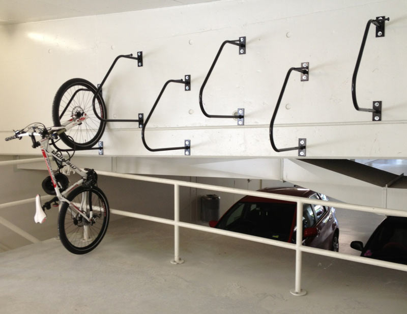 Vertical bike mounted on a black metal wall rack with multiple hooks in a parking garage setting