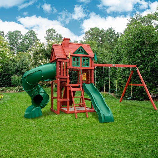 Cedar wooden swing set with two slides, climbing wall with rope, trapeze and belt swings, playhouse with shutters, and sandbox area.