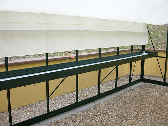 Royal Victorian Shade Curtains in beige fabric, partially lowered inside a green metal frame greenhouse structure