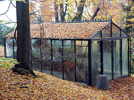 Classic English-style glass greenhouse with black metal frame, pitched roof, and surrounded by autumn leaves.