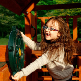 Child playing with green heavy-duty plastic ship's wheel attached to wooden swing set accessory