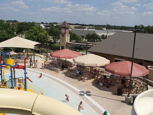 Single post umbrella shade structures in beige and red at a water park poolside with lounge chairs and visitors