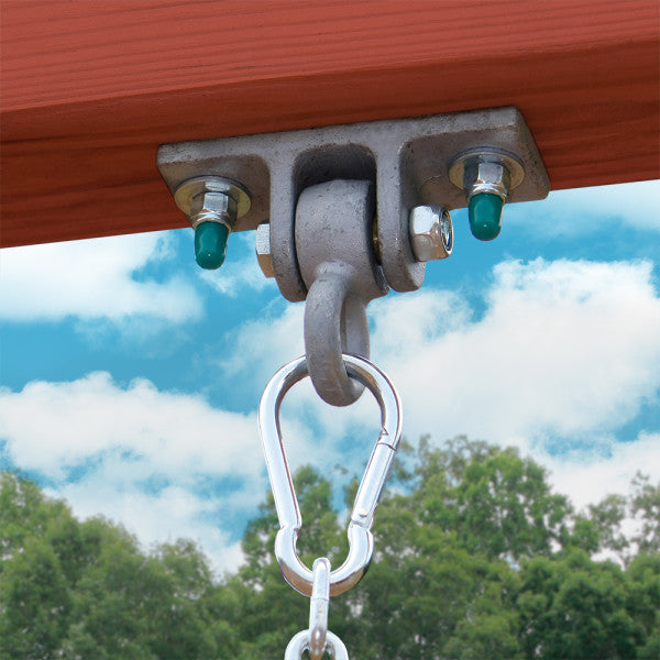 Metal swing hanger with carabiner attached to redwood-stained cedar beam of wooden swing set against blue sky and trees