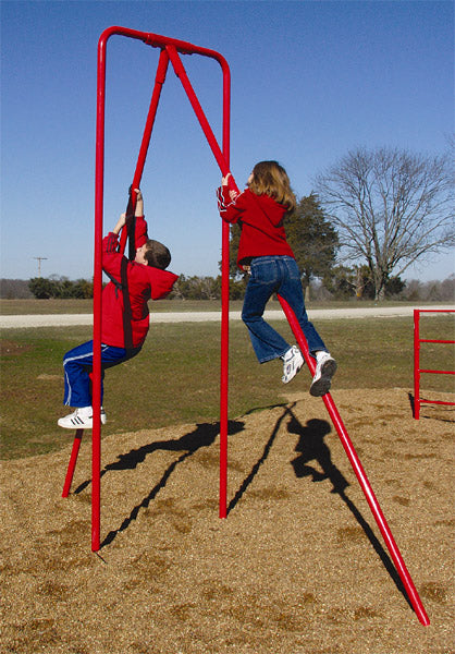 Two children climbing a red metal pole structure on an outdoor playground with wood chip ground and clear sky