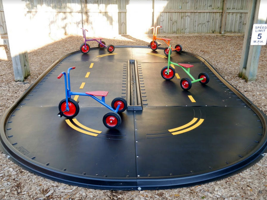 Curved black trike path with yellow markings and four colorful children's tricycles on playground surface