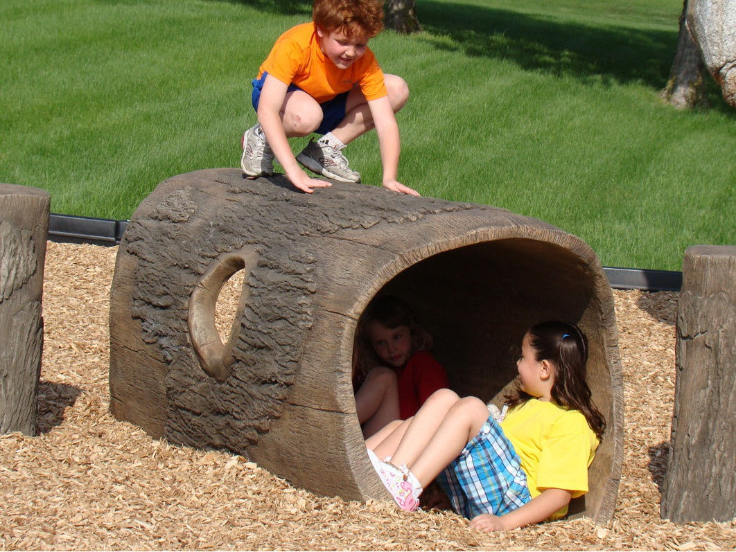 A child climbing on top of a nature-themed log tunnel playground climber.