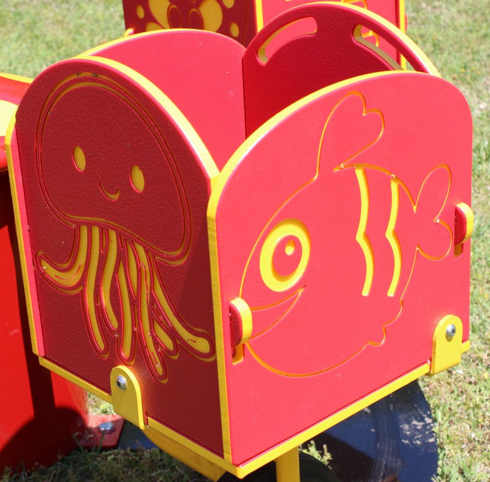 Red and yellow children's carousel seat with smiling jellyfish and fish figures on panels, outdoor playground equipment