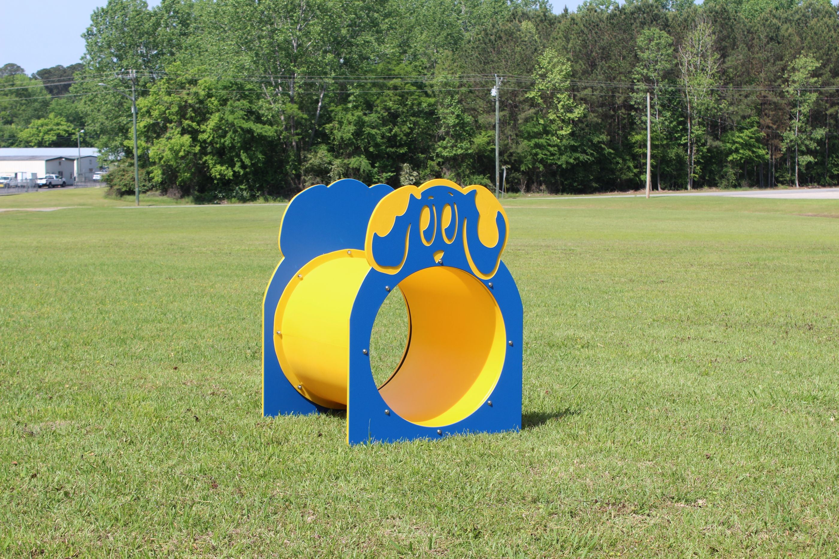 Blue and yellow dog agility tunnel on a grassy field with trees in the background