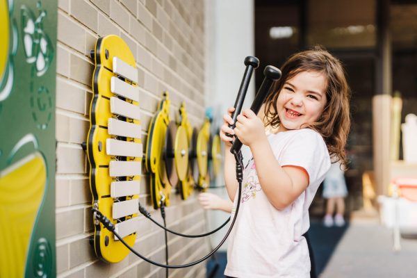 Child holding mallets while playing the wall-mounted Harmony Hive instrument