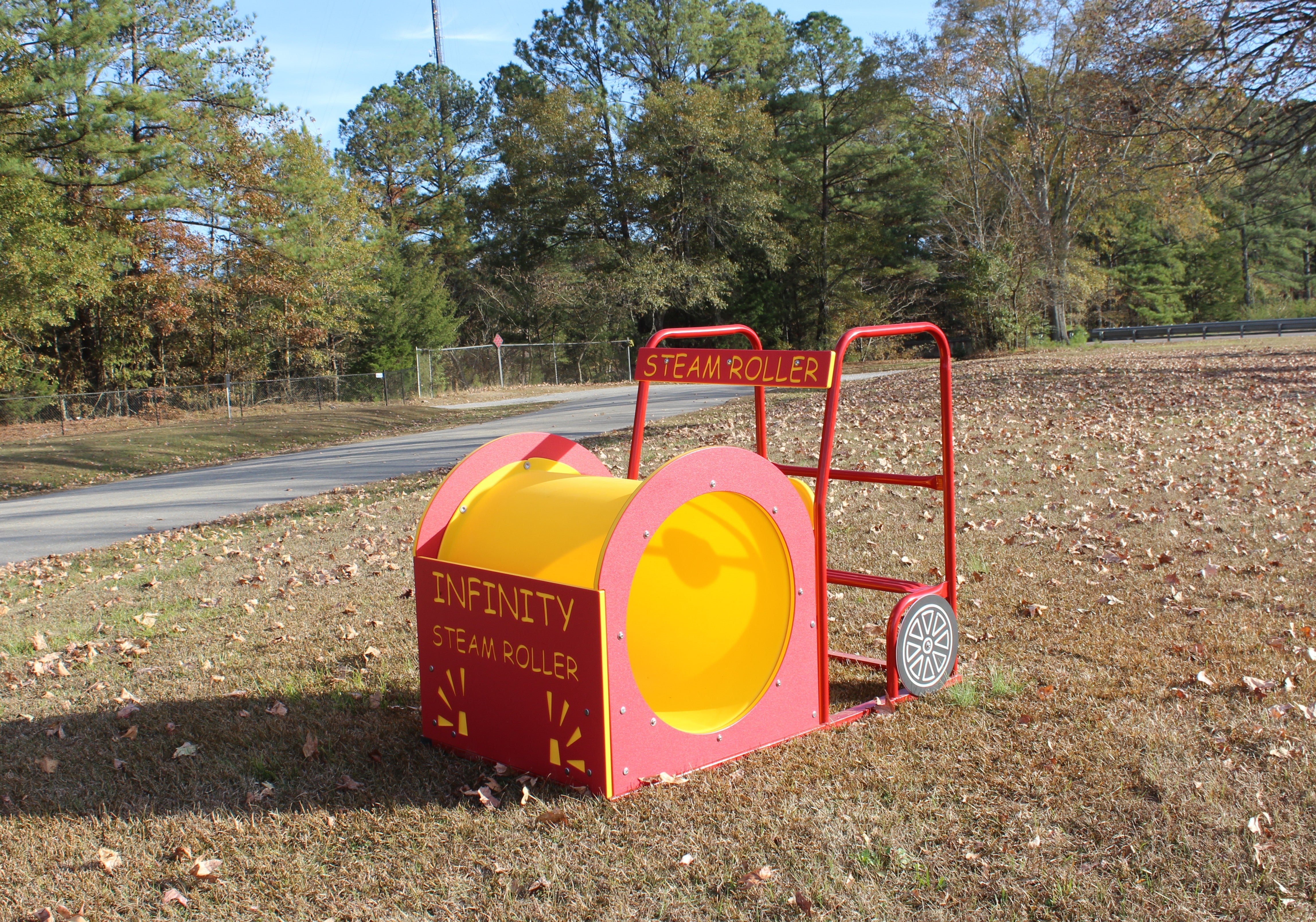 Bright yellow and red playground steam roller play structure with ladder and wheel details on grass