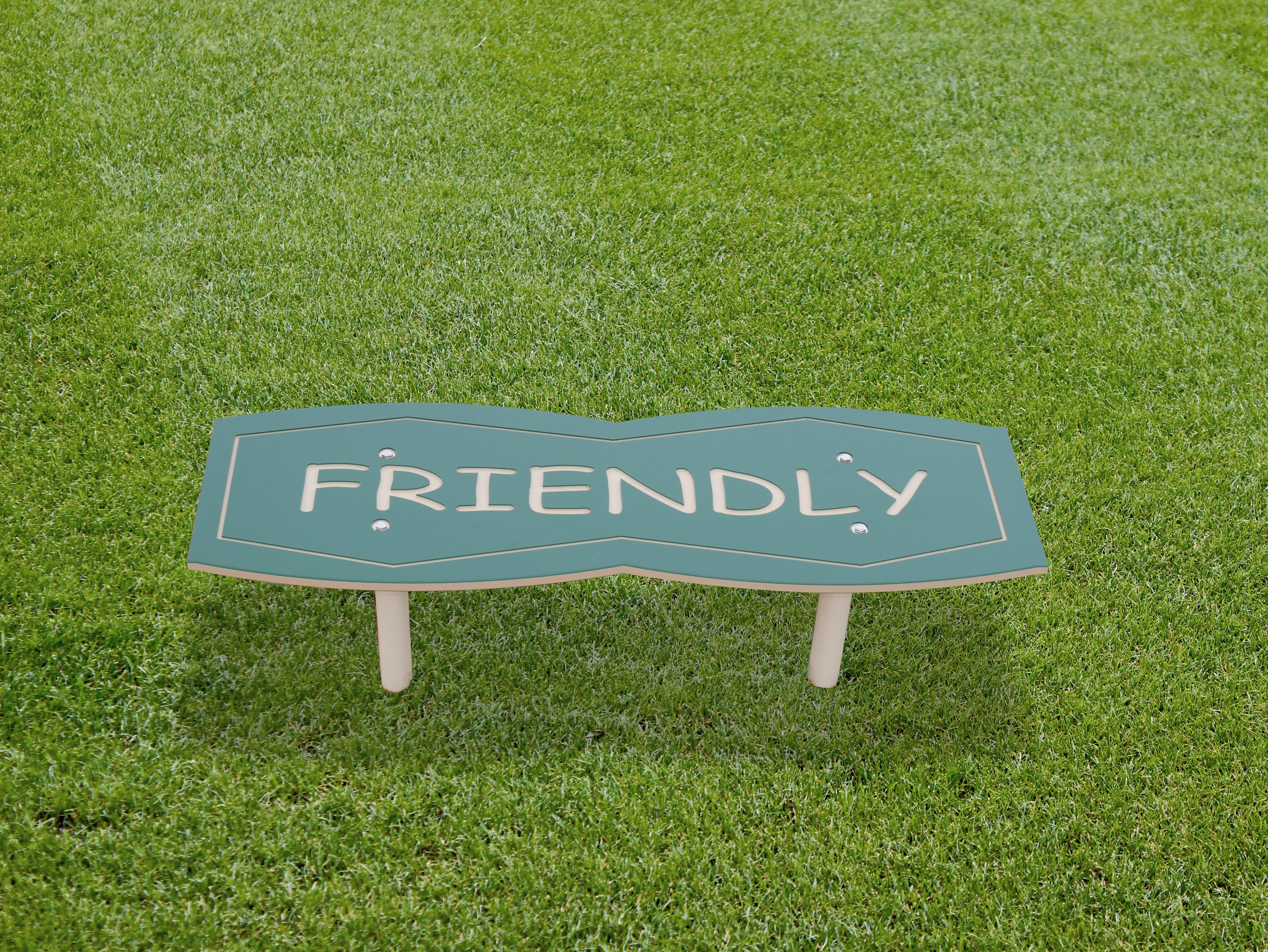 Green outdoor park bench with smooth edges and the word "Friendly" on the seat, designed for playgrounds and social-emotional learning.