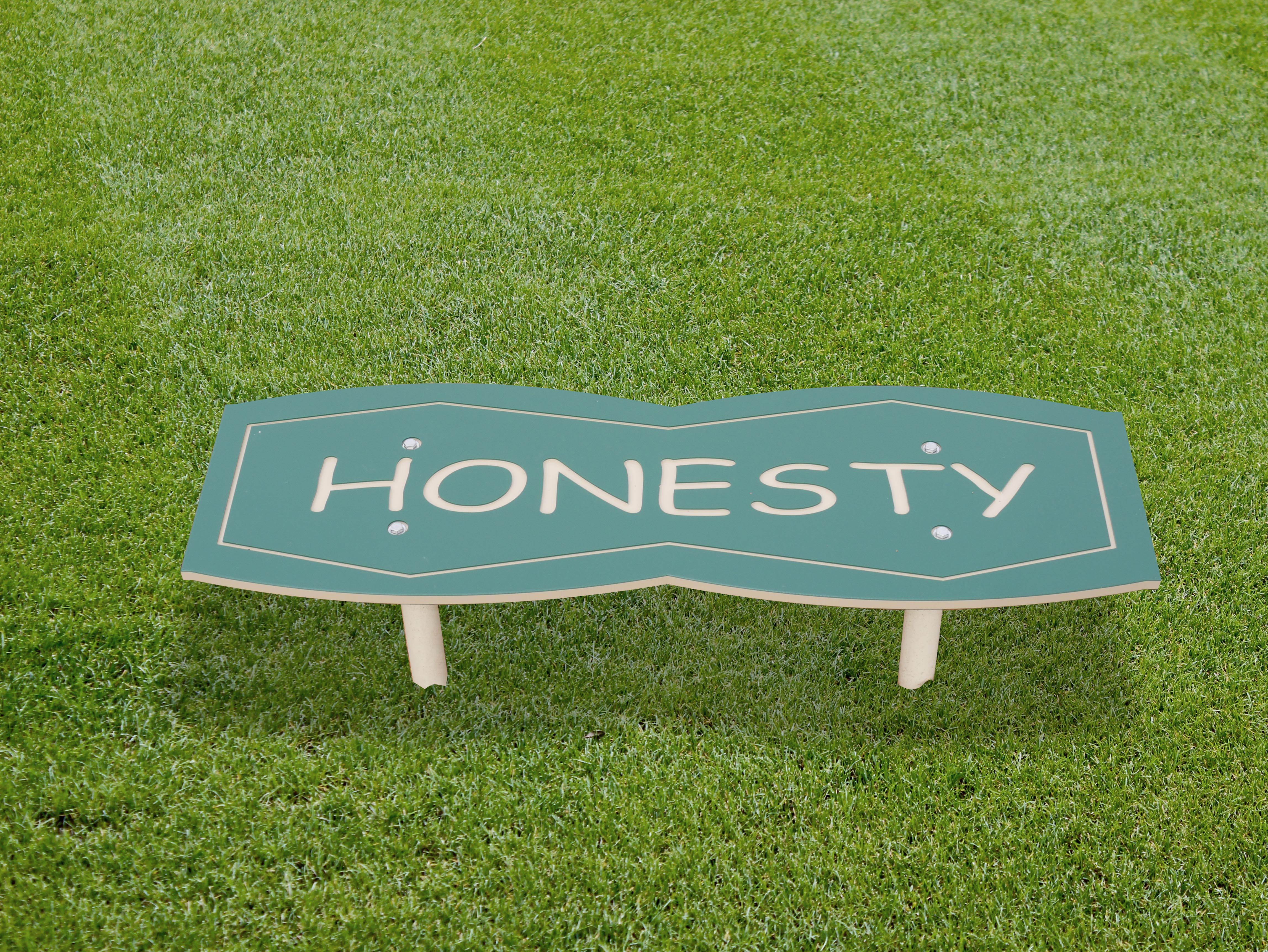 Green outdoor character bench with smooth edges and bold lettering promoting honesty, set on grass in a playground or park setting.