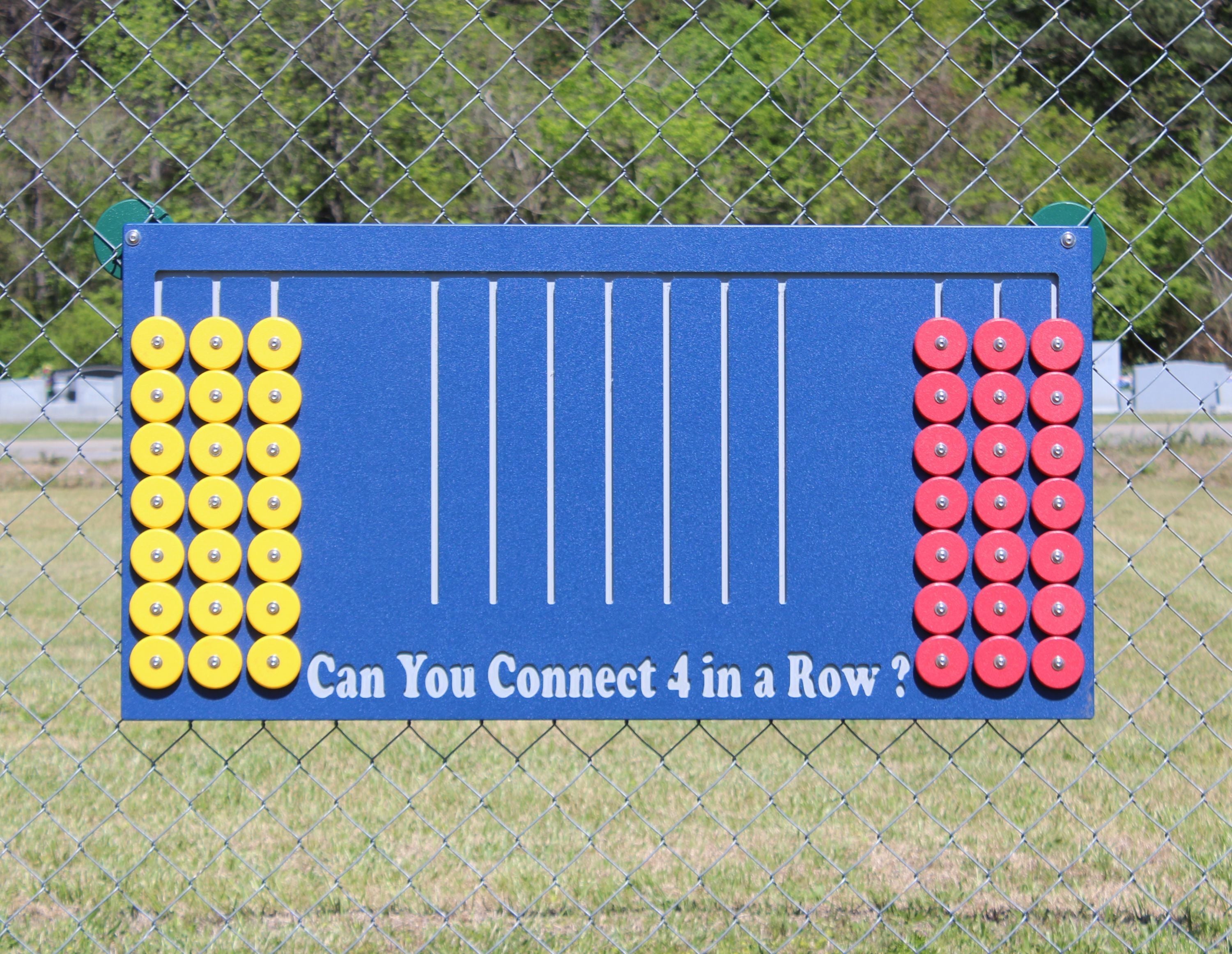 Outdoor Connect 4 game panel with yellow and red circular pieces on a blue board mounted on a chain-link fence
