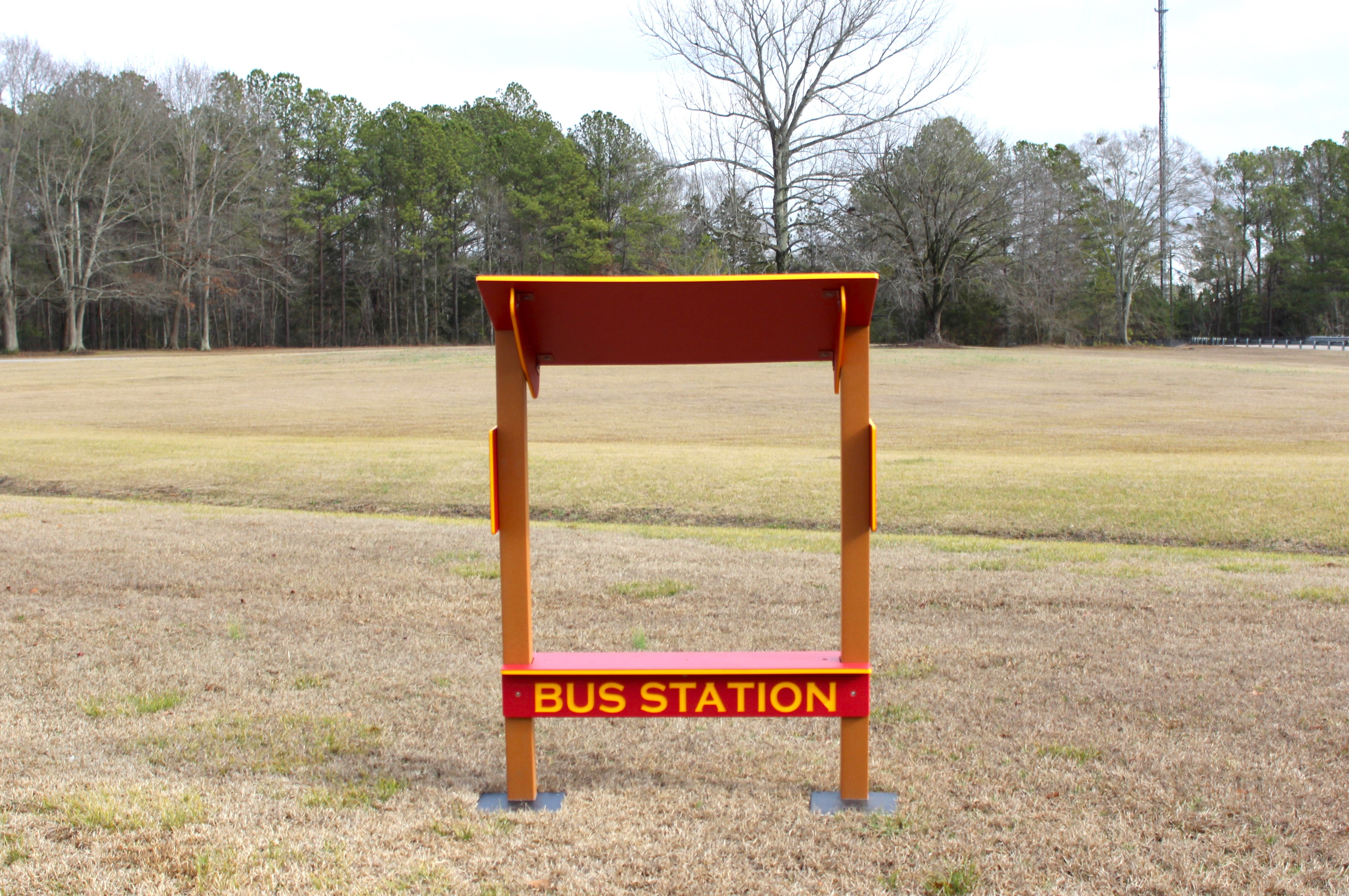 Red and orange outdoor playground bench with shaded top and bold yellow lettering, designed for imaginative bus stop play