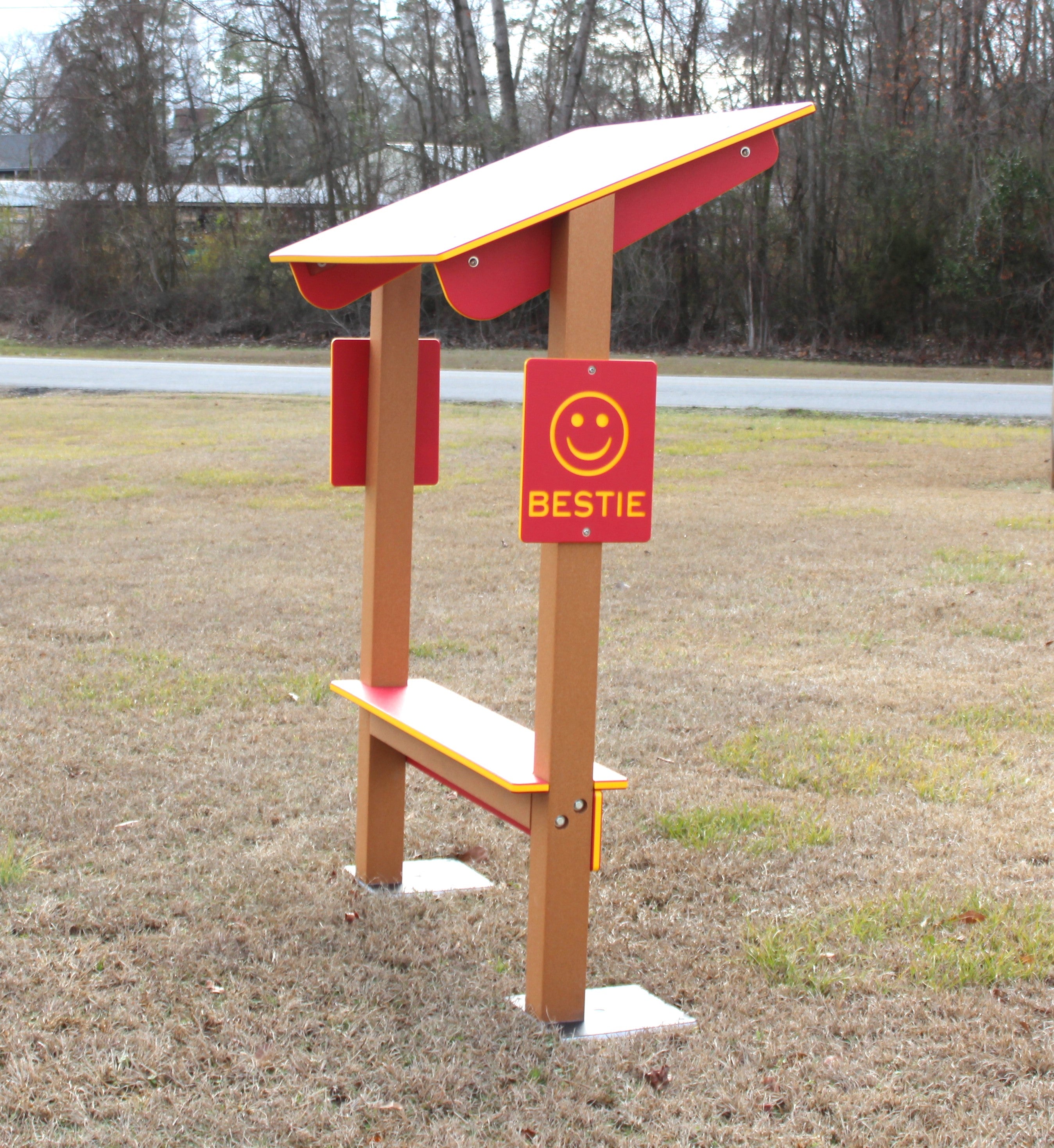 Outdoor playground bench with red panels, smiley face signage, and a slanted roof providing shade