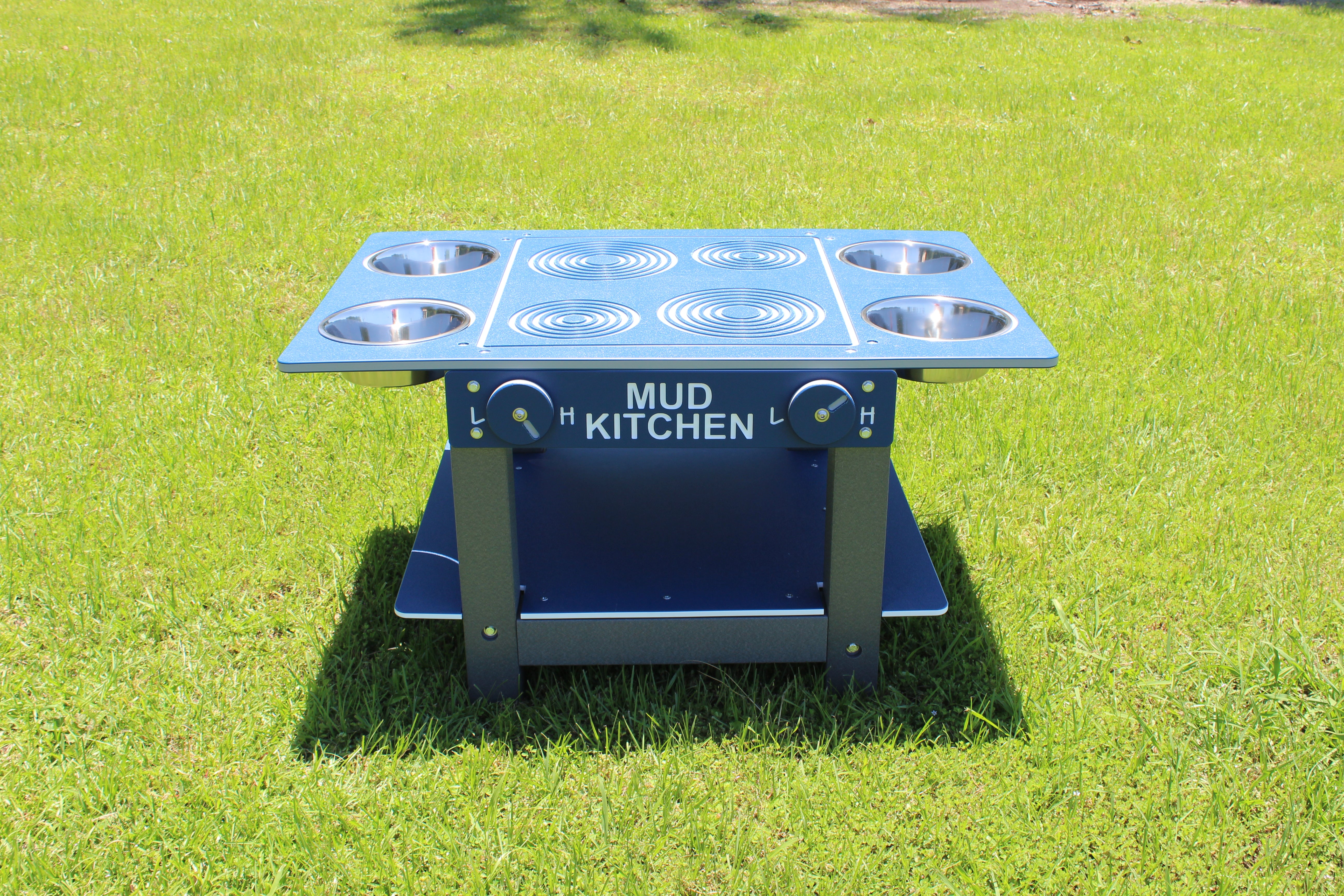 Blue and gray outdoor mud kitchen with four metal bowls, two knobs, and stove-top design on grass