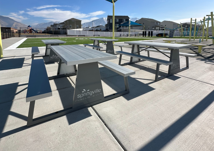 Outdoor picnic tables with powder-coated steel frames, recycled plastic planks, and custom logo panels in a park setting