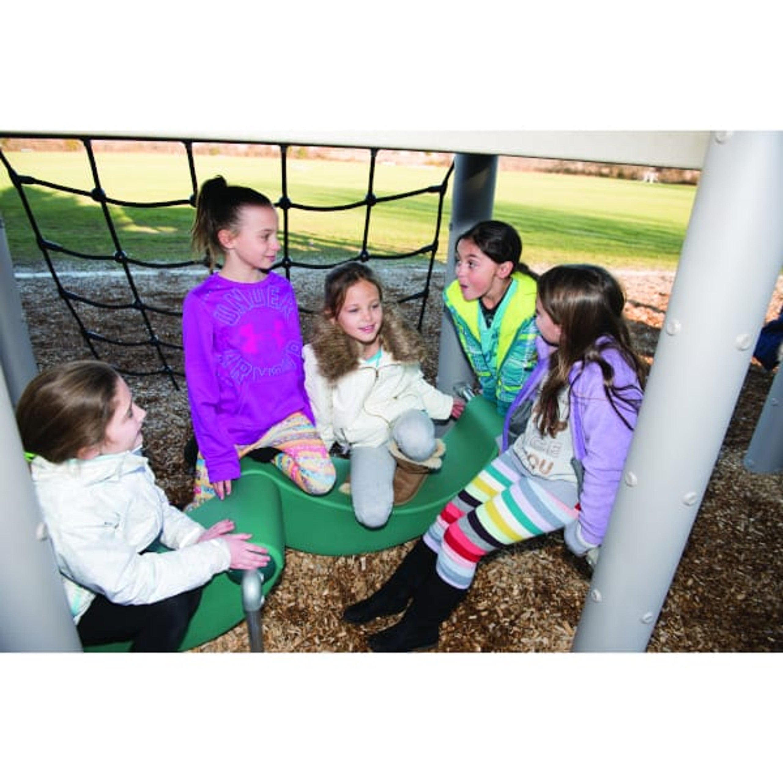 Five children playing on a green curved climbing structure beneath a rope net on a playground with integrated physical activities