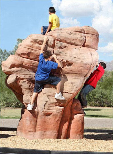 Children climbing on a large sandstone boulder in a playground setting.